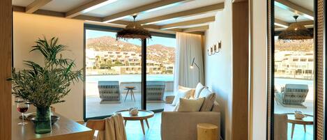A modern living room with a sofa, a dining table, and a large window offering a view of buildings and hills.