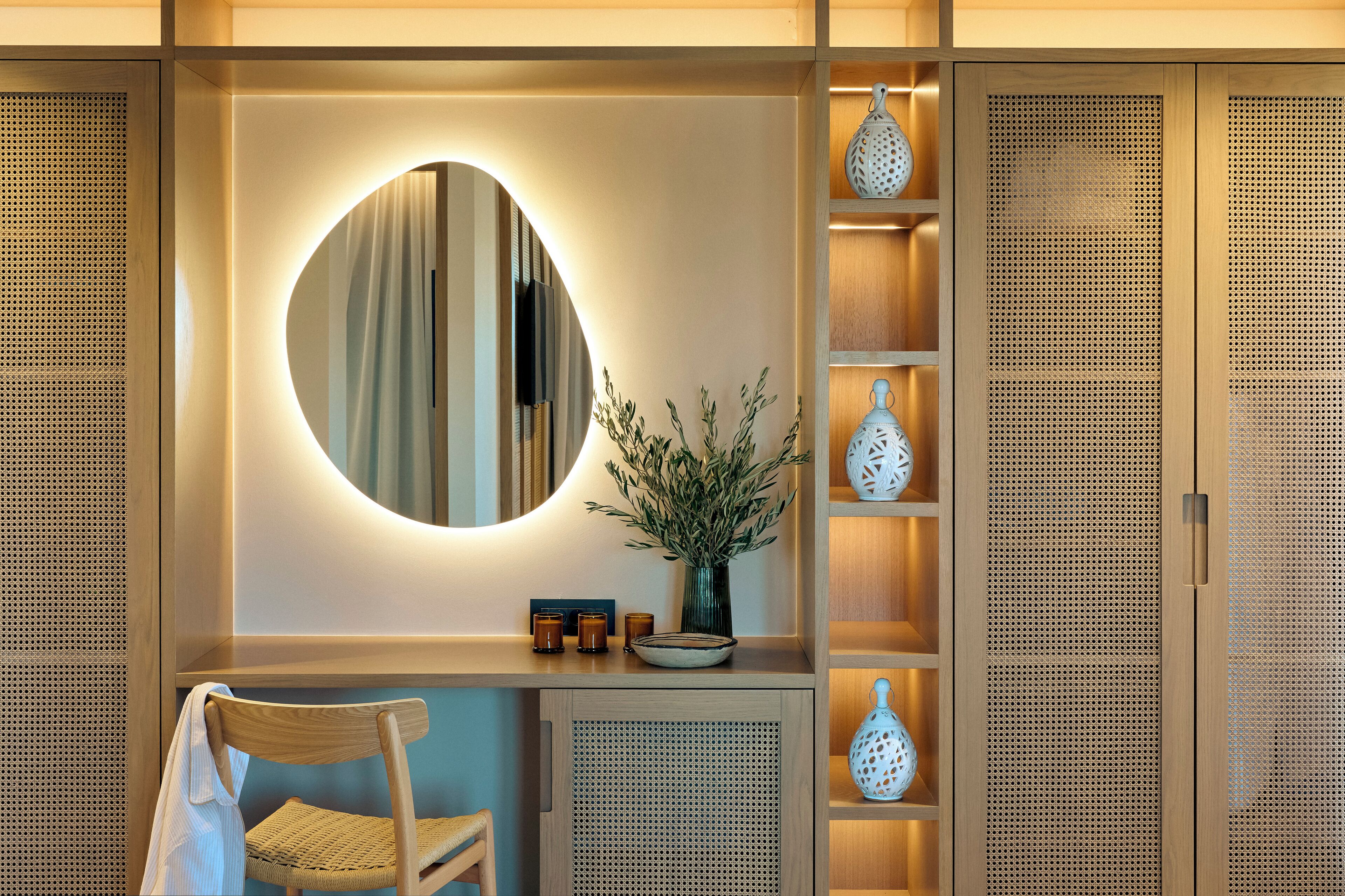 Un tocador moderno con un espejo redondo, un florero con follaje y un mueble de madera con estantes.