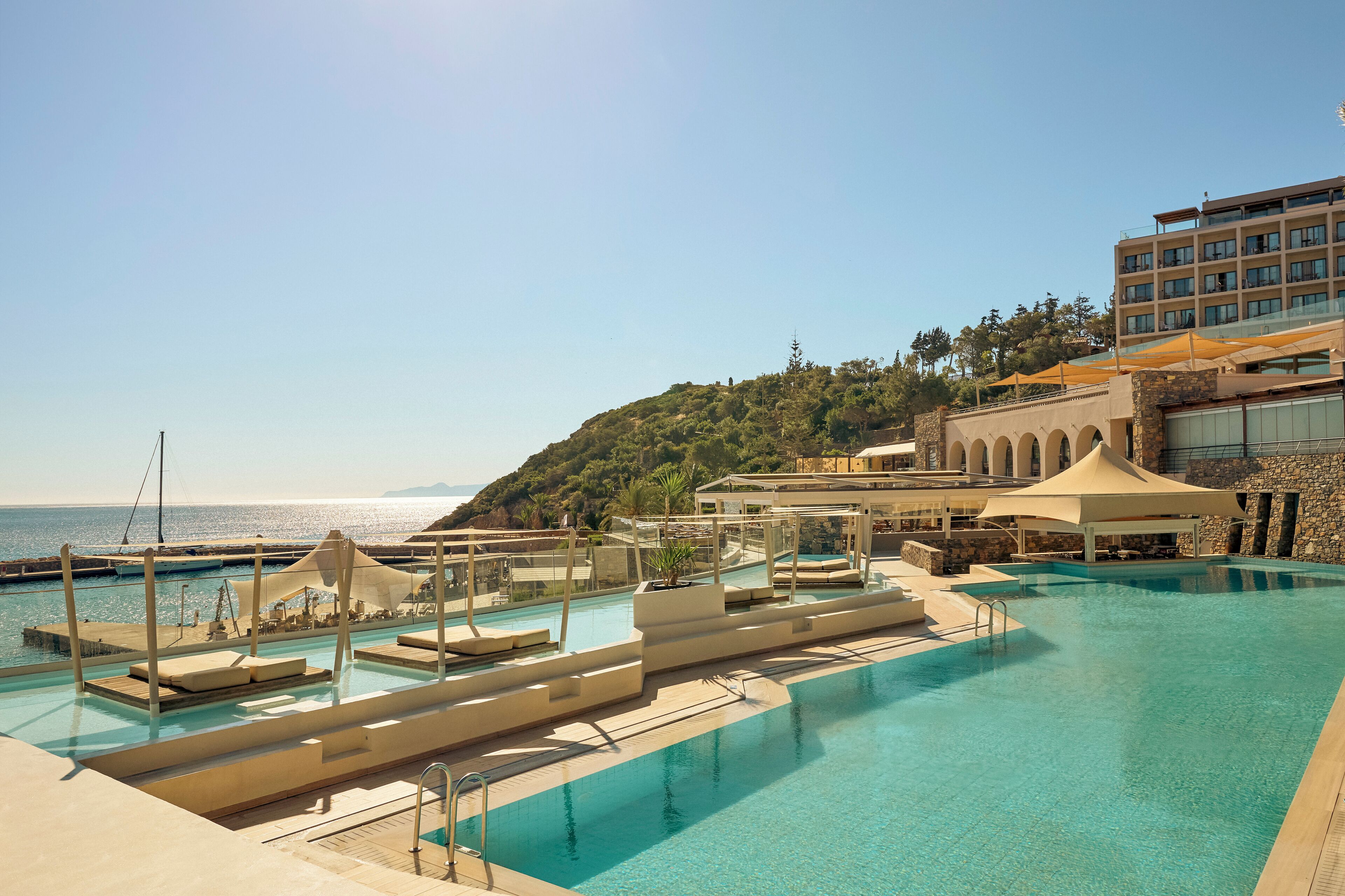 A pool area with clear blue water, sun loungers, and a view of the sea.