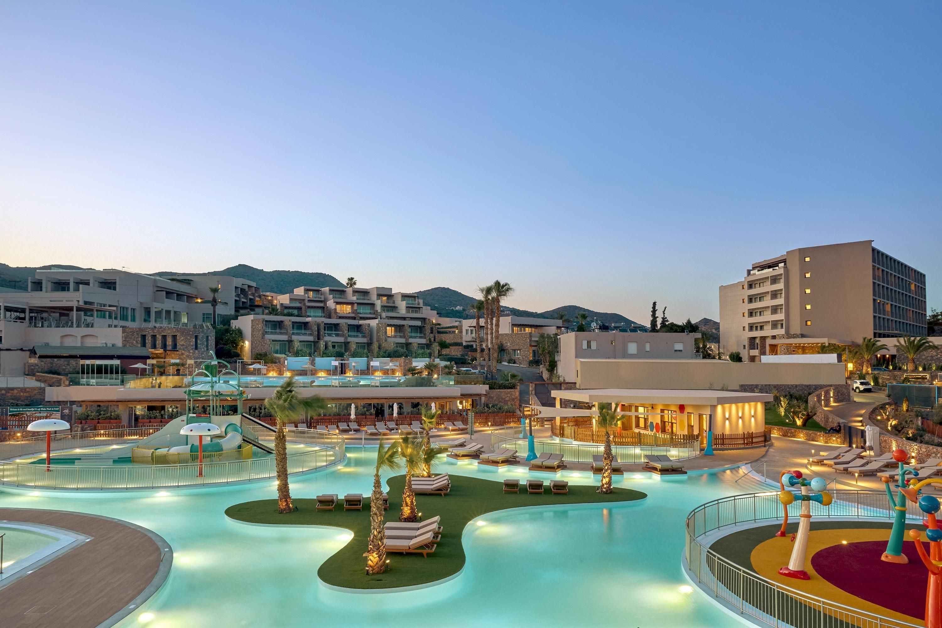 A resort with multiple swimming pools, lounge areas, and a mountainous backdrop.