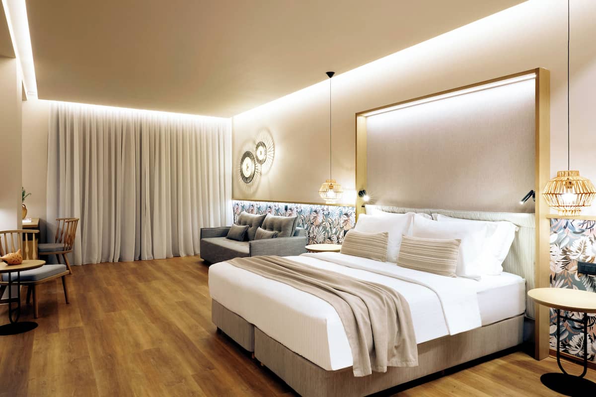 Una habitación de hotel moderna con una cama grande, un área de descanso con un sofá y sillones, una mesita y un adorno en la pared.