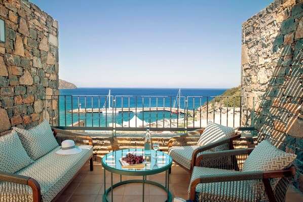 A balcony with wicker furniture, a glass table, and a view of the sea and a small island. - Zeus Eleva Mirabello Bay (Agios Nikolaos)