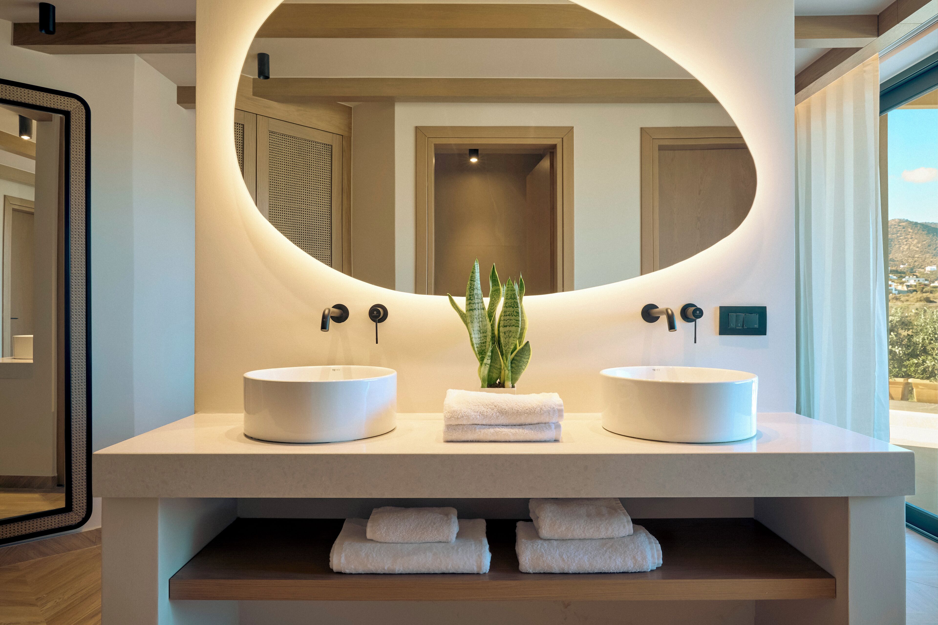 A modern bathroom with two round sinks, a large mirror, and a small plant.