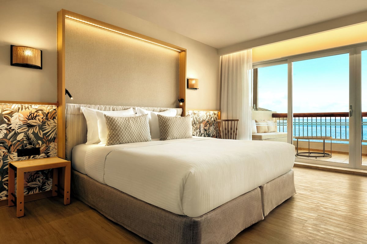 Un dormitorio espacioso con una cama grande, una mesita de noche y vistas al mar desde un balcón.