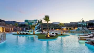 Relax by the resort's large pool, featuring multiple lanes and a central slide, surrounded by lush greenery and palm trees.