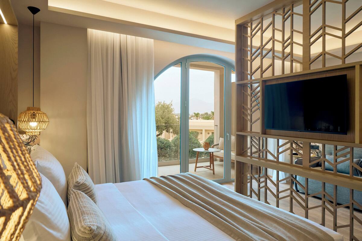 Habitación de hotel con cama, cortinas, televisor y balcón con vistas.