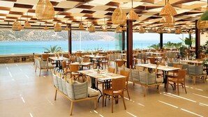 Un restaurant spacieux, doté de nombreuses tables et chaises, de grandes fenêtres donnant sur la mer et de lampes en osier suspendues au plafond.