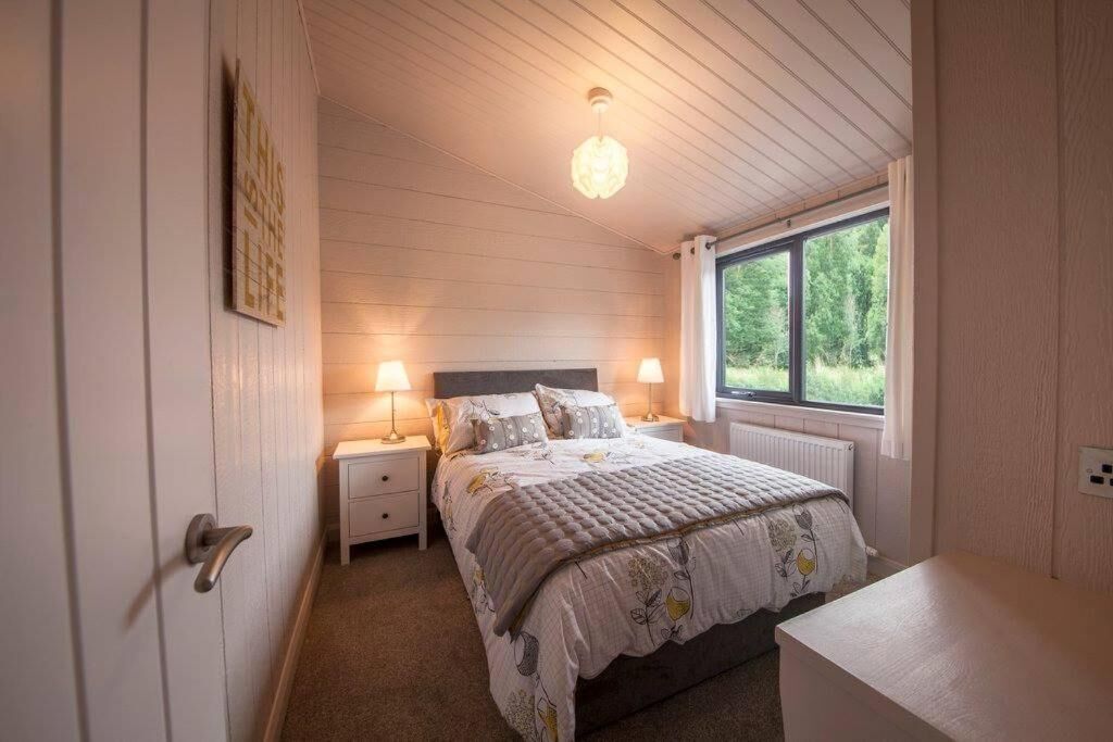 Quarto com cama, luminárias de cabeceira, uma janela e uma porta.