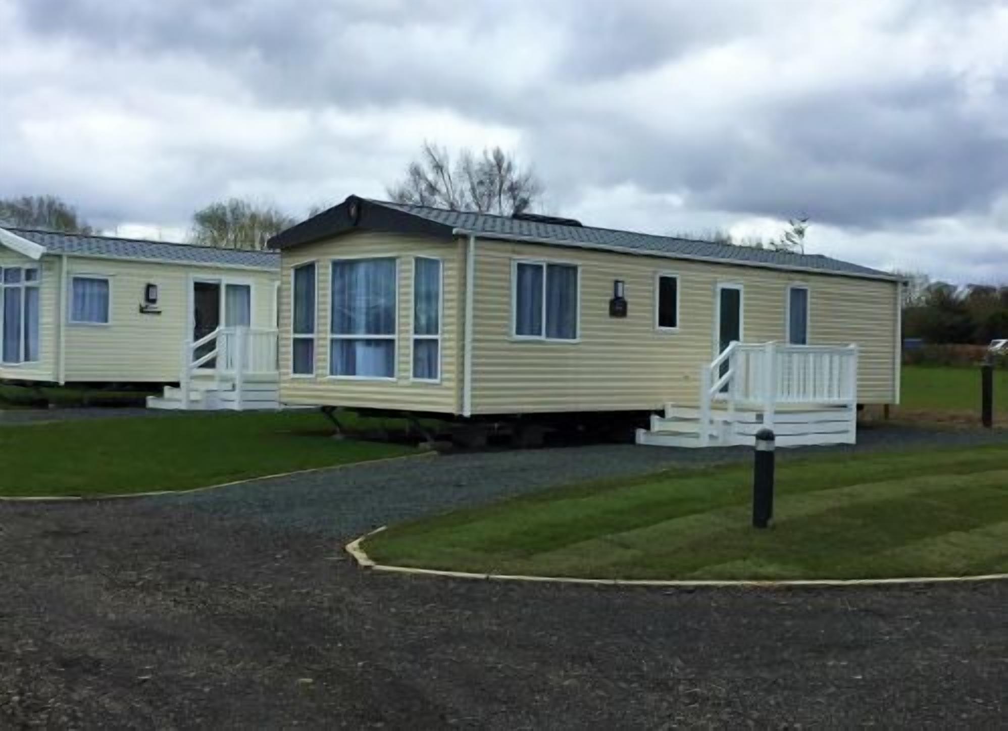 A row of mobile homes with a grassy area in front and a gravel path leading to the entrance.