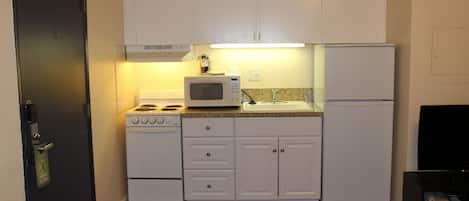 Cocina compacta con armarios blancos, microondas, estufa y refrigerador.