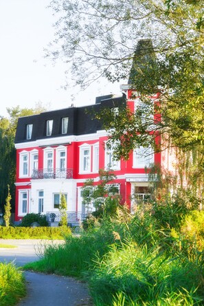 Ein rotes und weißes Gebäude mit zahlreichen Fenstern und Balkonen, umgeben von viel Grün.