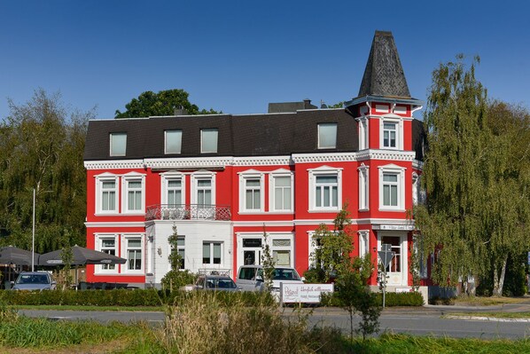 A red and white building with a prominent tower, likely a hotel, featuring multiple windows and a sign indicating it is a hotel and restaurant. - Peters Das Genusshotel in der Wingst (Wingst)