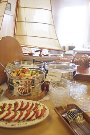 A buffet table with various food containers and a sailboat model in the background. - Peters Das Genusshotel in der Wingst (Wingst)