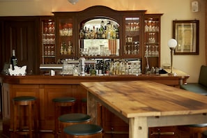 A bar area with wooden cabinets, stools, and a long wooden table.