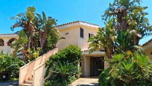 A two-story building with a beige facade, a tiled roof, and a staircase leading to the entrance. - Porto Giunco (Villasimius)