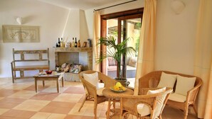 A cozy living room with a checkered floor, wicker furniture, a fireplace, and a view through a glass door. - Porto Giunco (Villasimius)