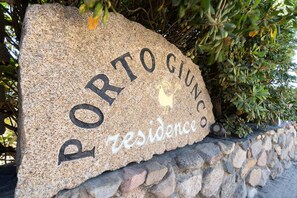Un letrero de piedra con la inscripción 'PORTOCIUNCO residence' y un símbolo de gallo.