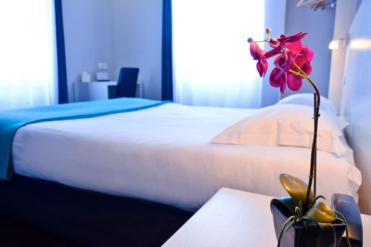 A hotel room with a bed, a desk, and a vase with a flower.
