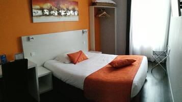 Habitación de hotel con cama, escritorio, silla, perchero y un cuadro en la pared.