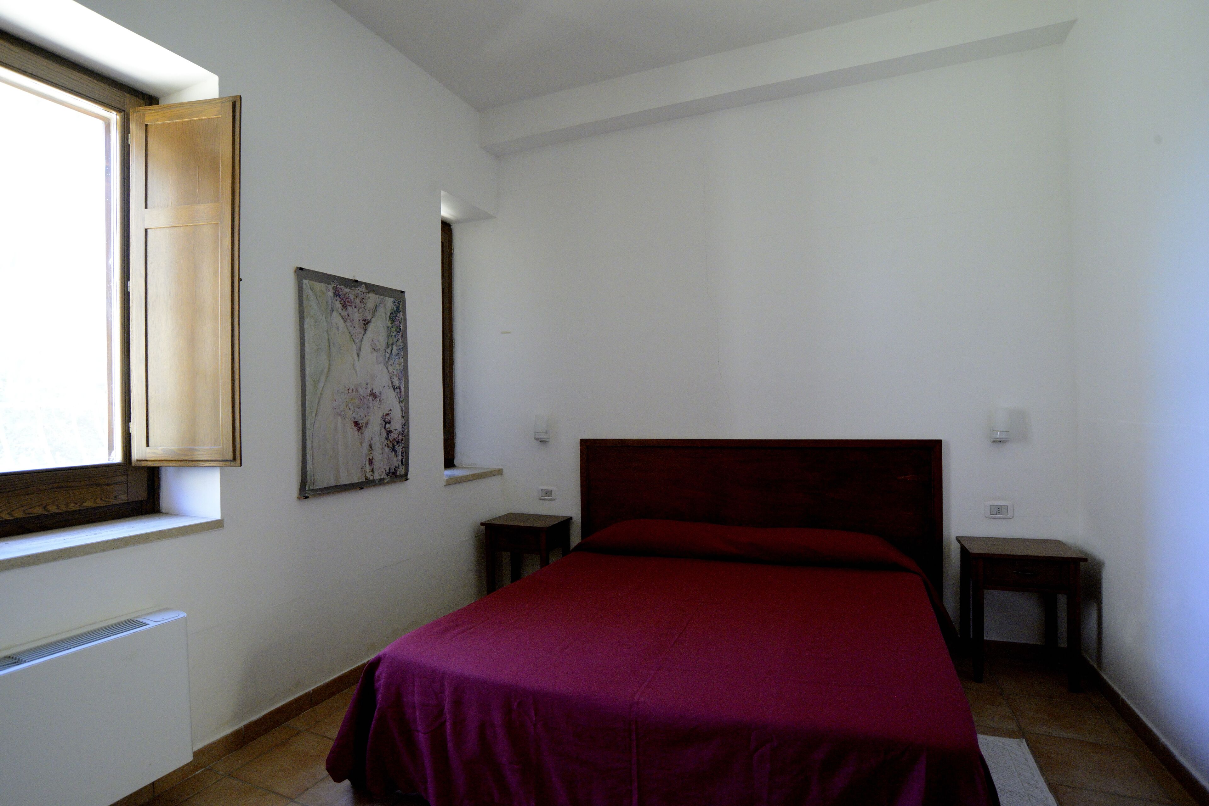 Une chambre avec un grand lit, une fenêtre, un radiateur et une petite table.