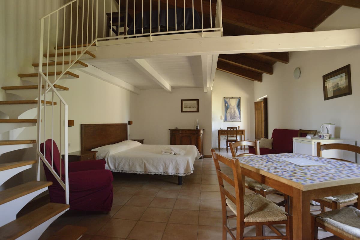 Ein Schlafzimmer mit einer Holztreppe, einem Bett, einem Schreibtisch und einem Esstisch.