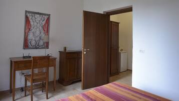 Una habitación con un escritorio de madera, una silla y un armario. Hay una puerta que conduce a otra habitación.