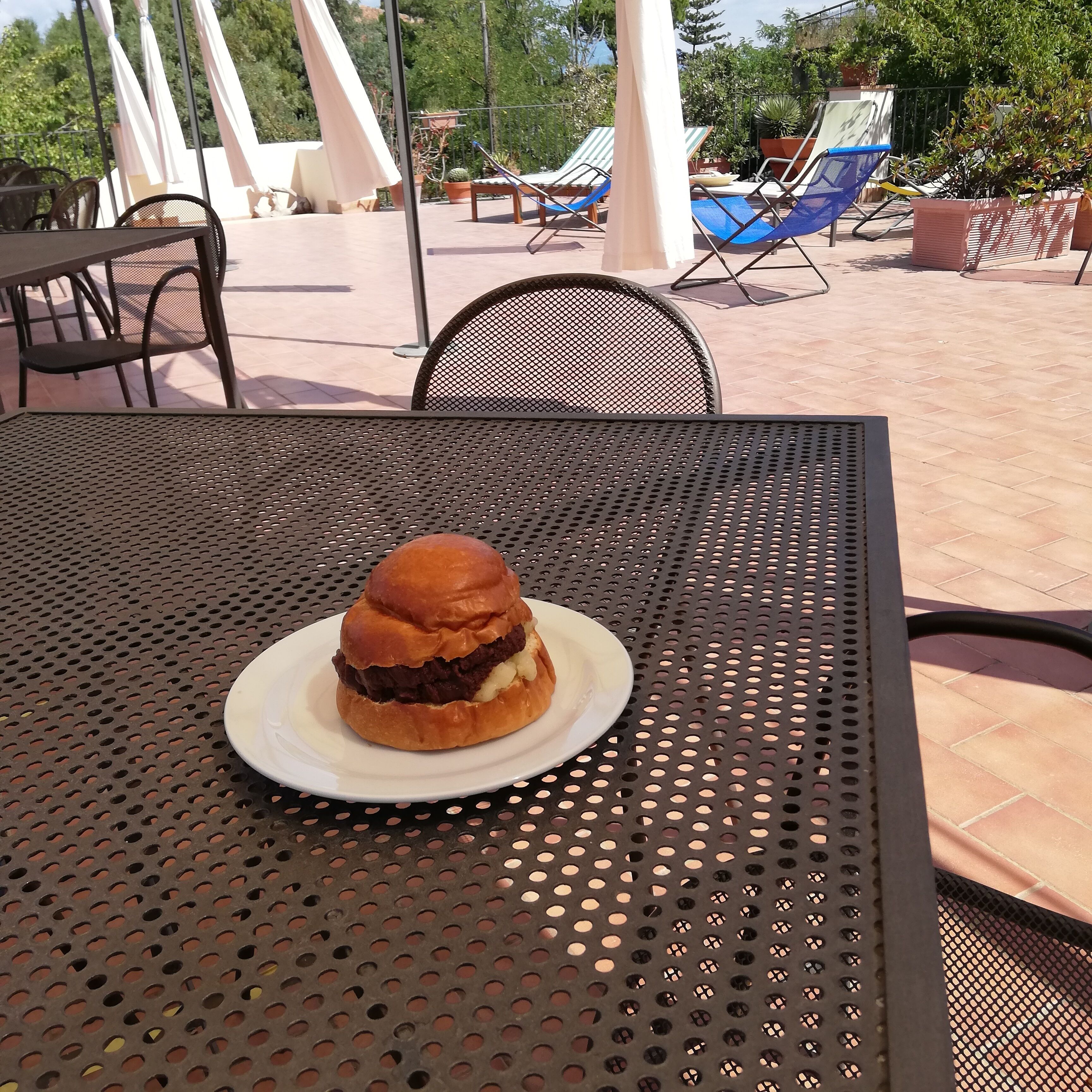 A table with a plate of food, outdoor seating with chairs and umbrellas, and a pool area in the background.