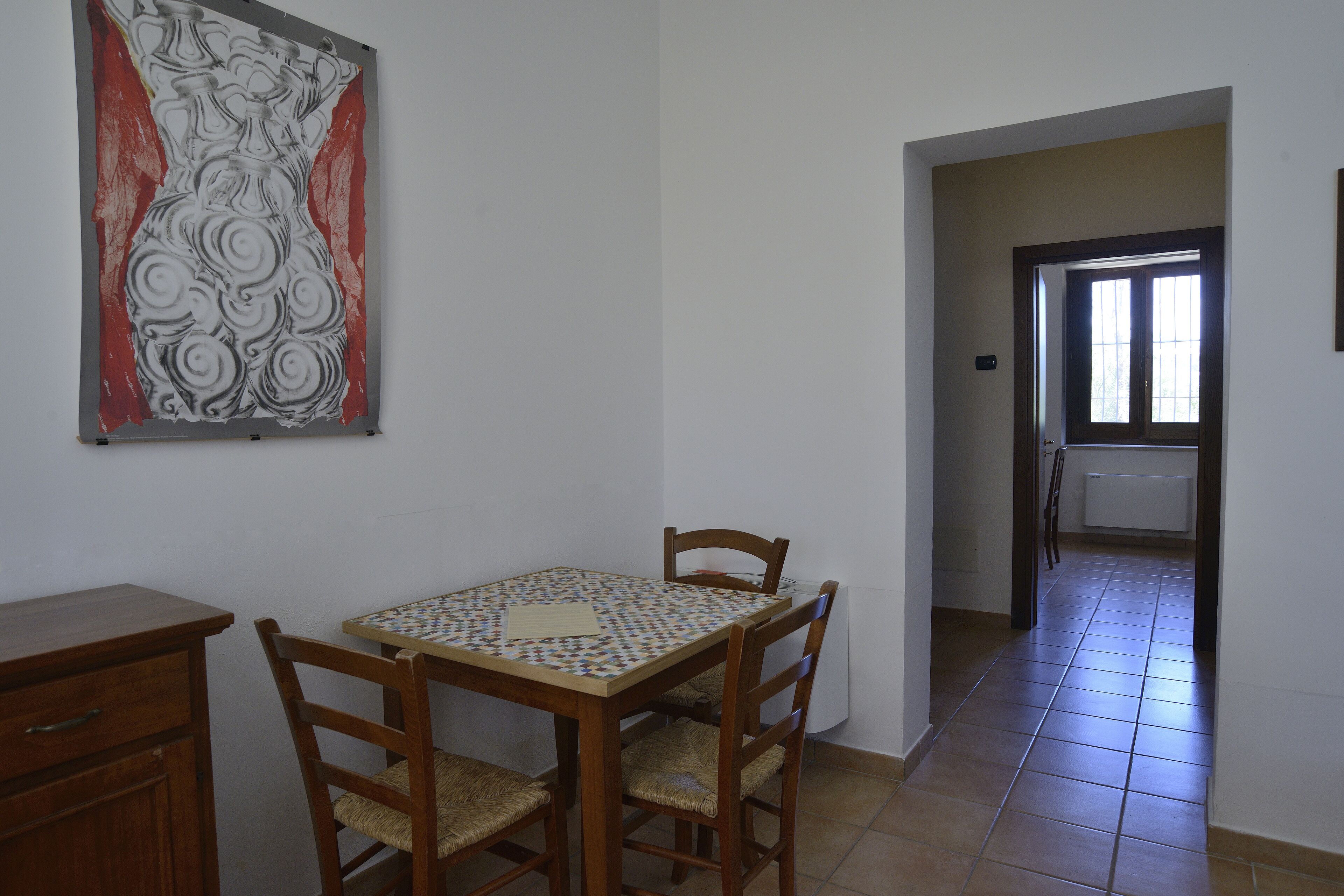 Un comedor con una mesa y sillas de madera, un mantel estampado y un cuadro abstracto colgado en la pared.