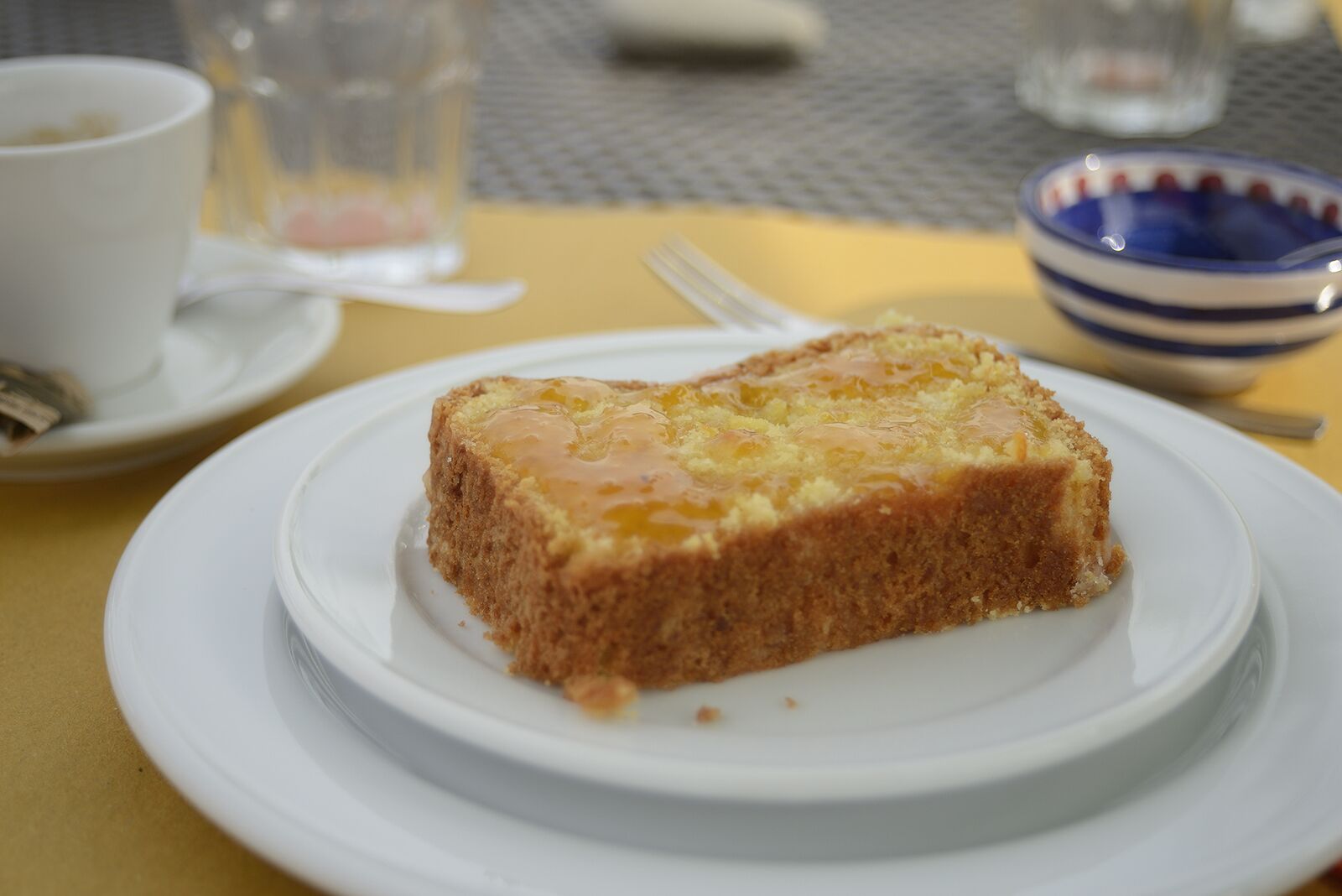 Una porción de pastel sobre un plato blanco, con un tenedor y una taza al fondo.