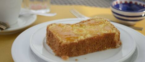 Una porción de pastel sobre un plato blanco, con un tenedor y una taza al fondo.