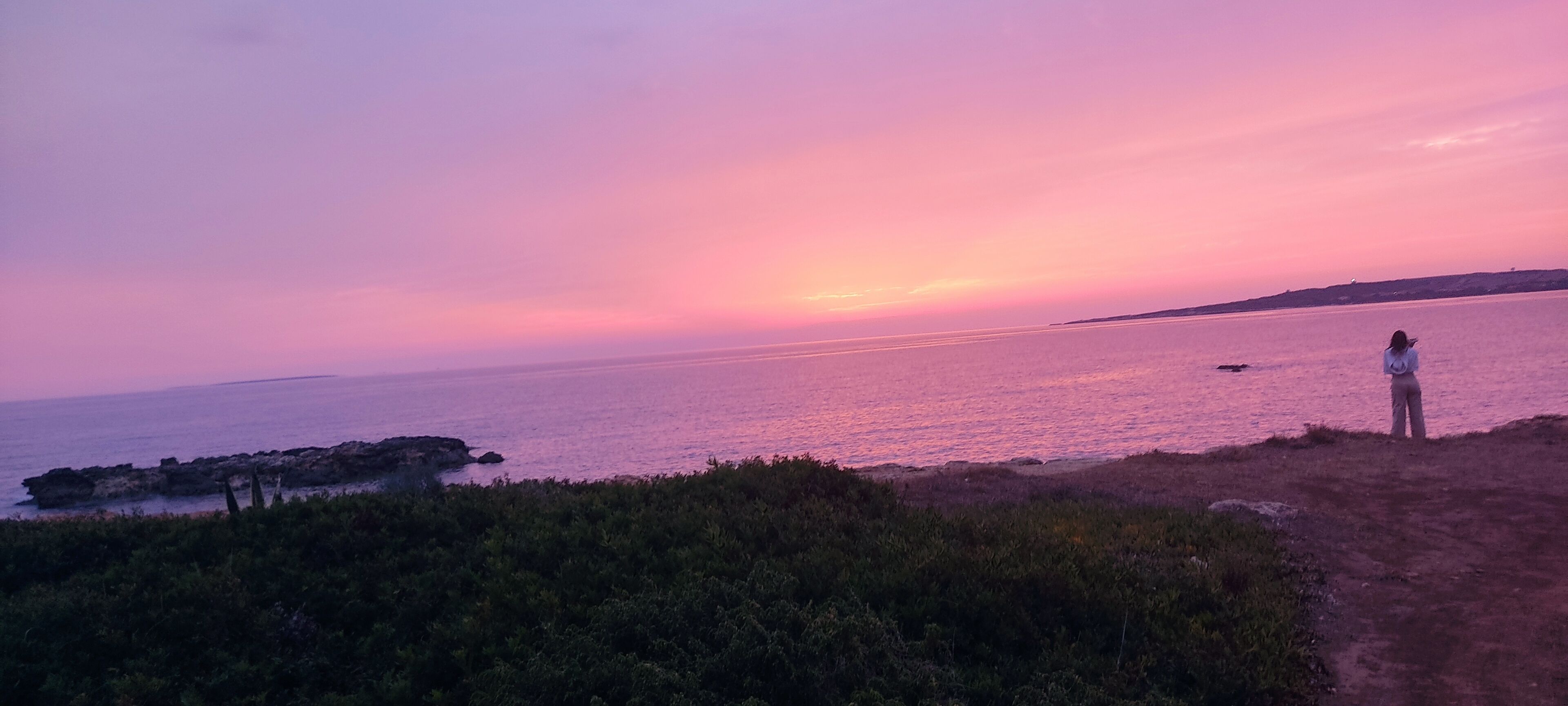Een kustlandschap met iemand die op een pad staat en de zee bezoekt tijdens zonsondergang.
