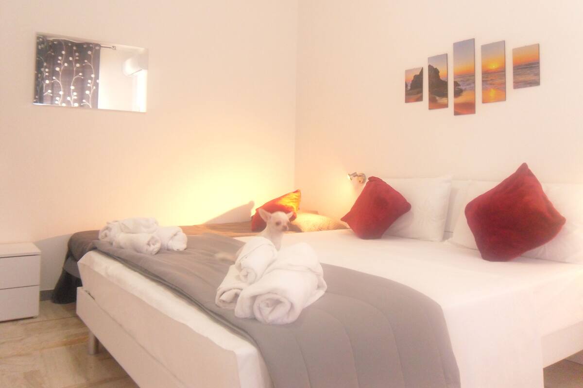 A hotel room with a bed, pillows, a nightstand, a lamp, and artwork on the wall.