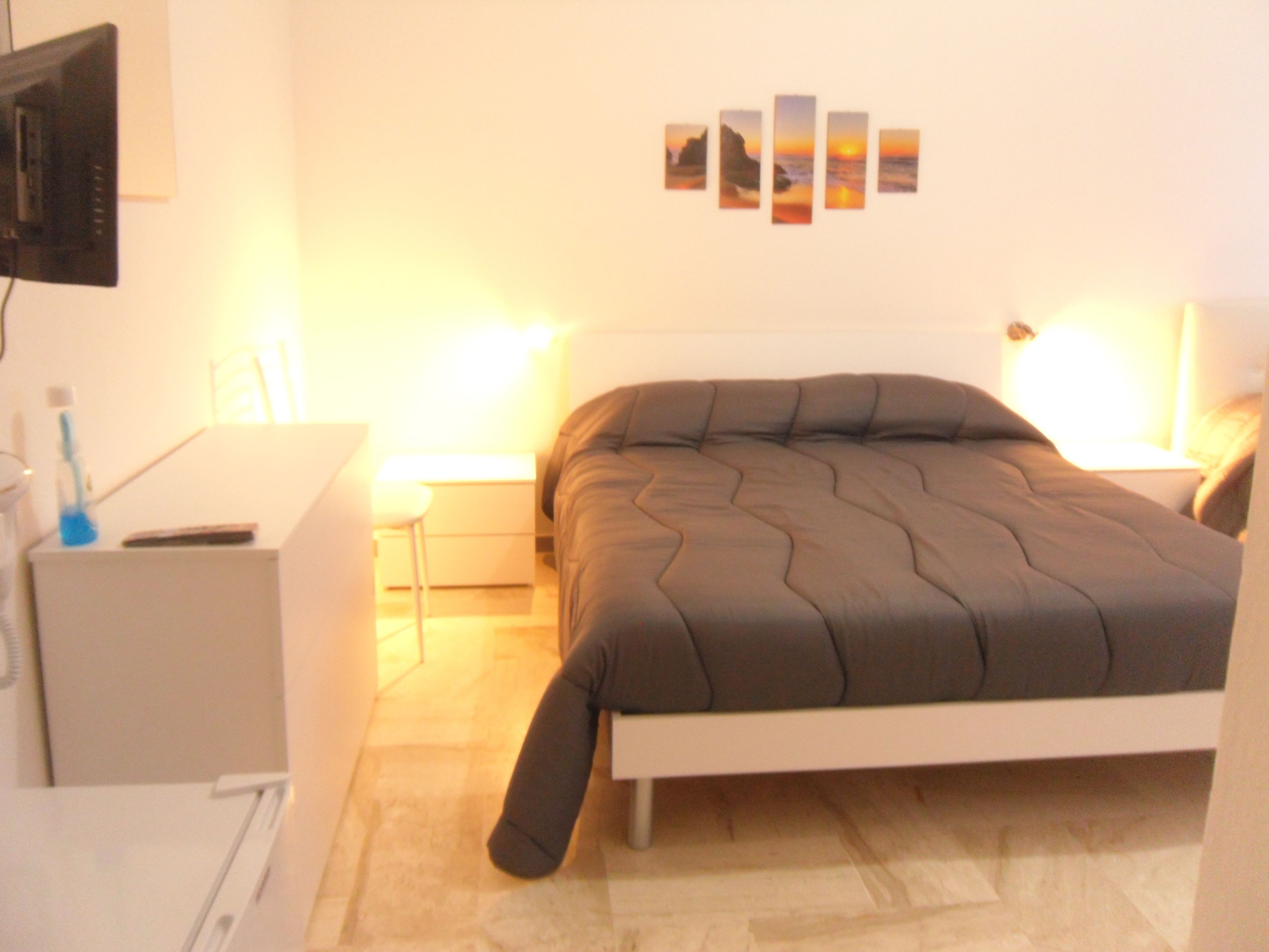 Une chambre à coucher avec un lit, des tables de chevet, une télévision et des œuvres d’art accrochées au mur.