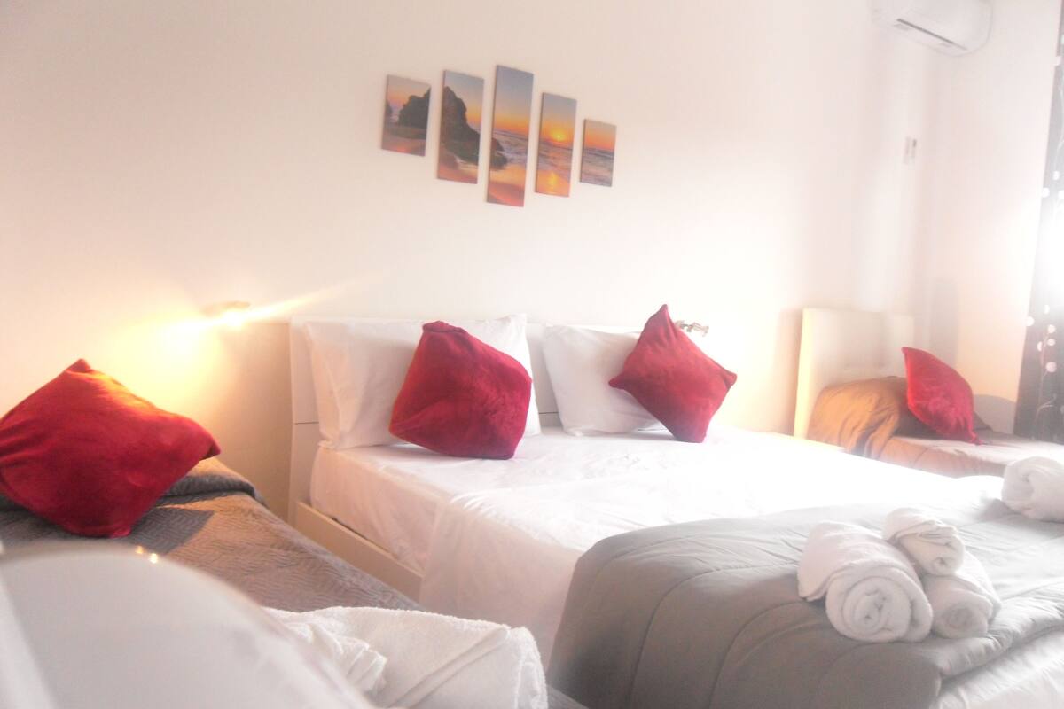A hotel room with two beds, white bedding, red pillows, a wall-mounted artwork, and a bedside lamp.