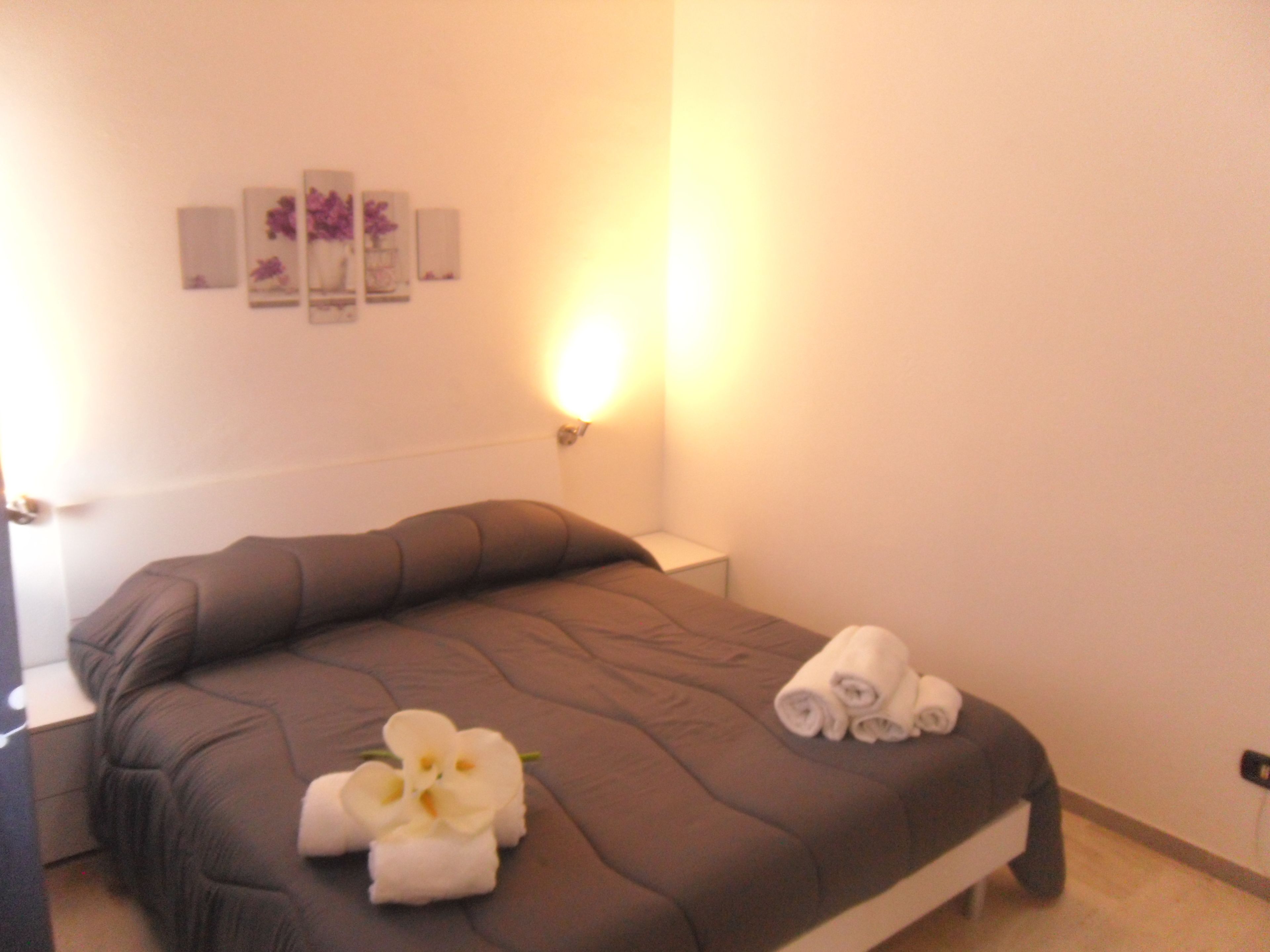 A neatly made bed with a brown bedspread, two rolled towels, and a white orchid decoration.