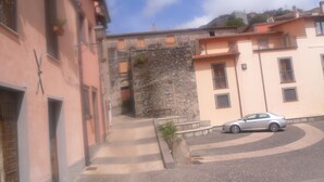 A narrow street with buildings on both sides, a stone wall, and a parked car. - B&B Italia (Milis)