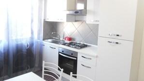 A compact kitchen with white cabinets, a gas stove, a sink, and a dining area with a table and chairs. - B&B Italia (Milis)