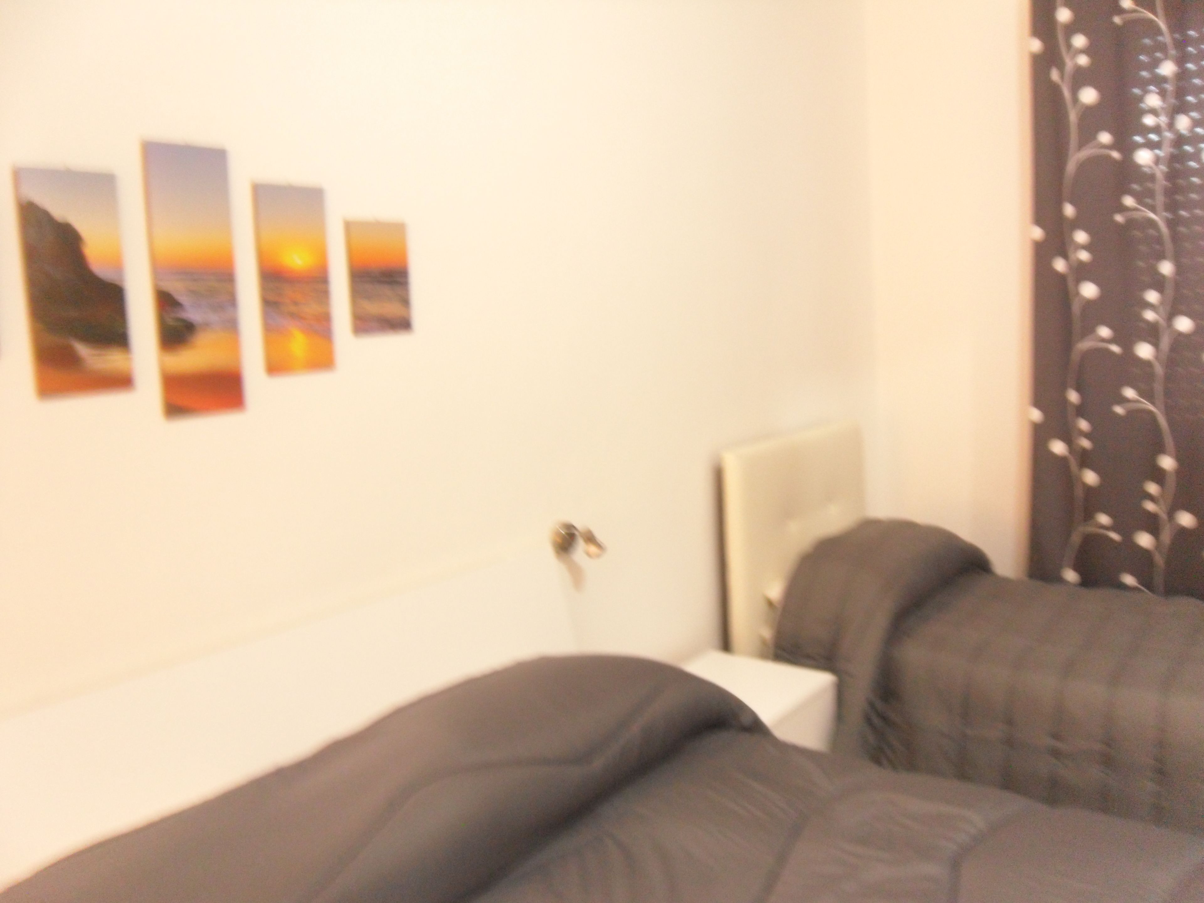 A hotel room with a bed, a bedside table, and a wall-mounted picture frame with four pictures.