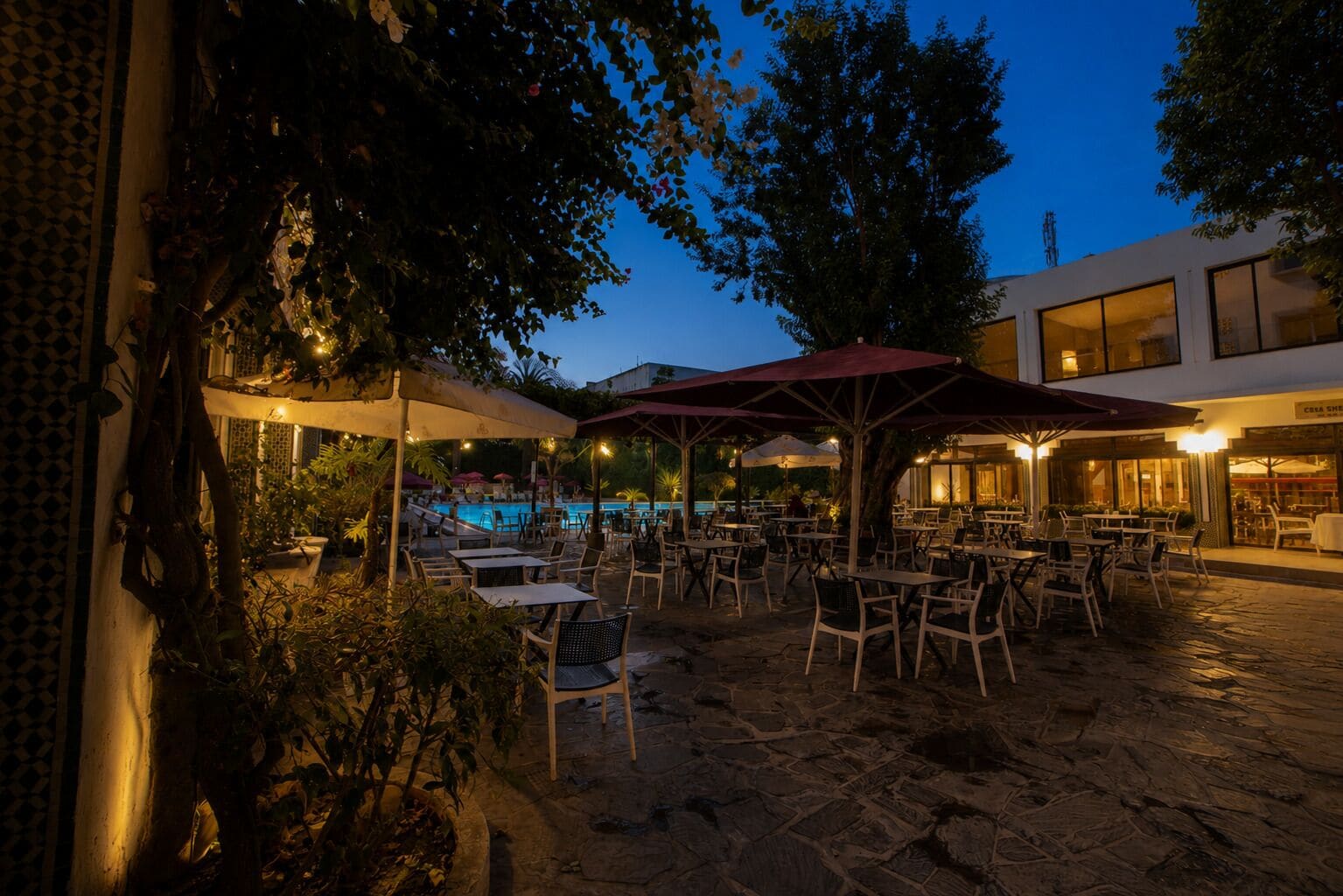 Un espacio al aire libre con mesas, sillas, piscina y sombrillas.