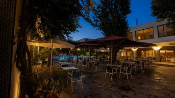 Un espacio al aire libre con mesas, sillas, piscina y sombrillas.
