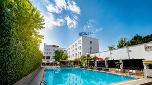 A hotel with a swimming pool, surrounded by greenery and a clear sky. - Hotel Mamora (Kenitra)