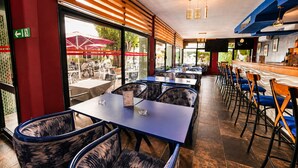 A restaurant with indoor seating, a bar area, and large windows offering a view of the outdoor seating area. - Hotel Mamora (Kenitra)