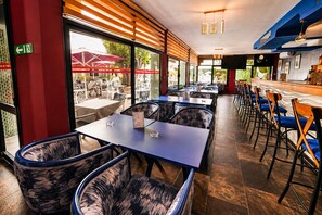 A restaurant with indoor seating, a bar area, and large windows offering a view of the outdoor seating area. - Hotel Mamora (Kenitra)
