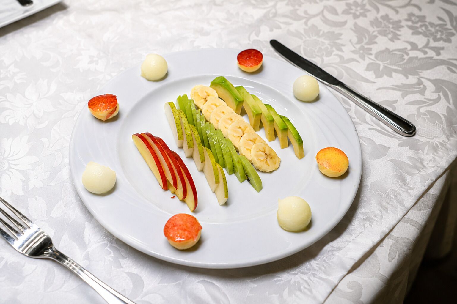 A plate with sliced fruits and a dessert on a tablecloth.