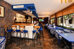 A bar area with a counter, bar stools, and a seating area with tables and chairs. - Hotel Mamora (Kenitra)
