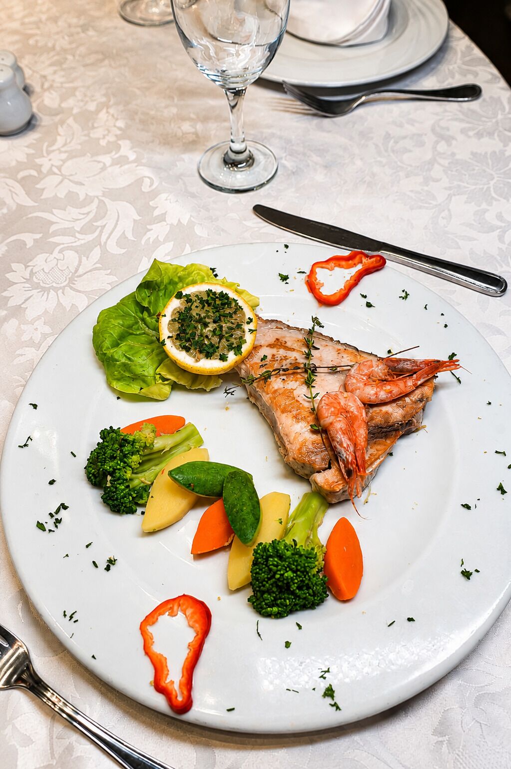 Un plato con pescado a la parrilla, verduras y una rodaja de limón.