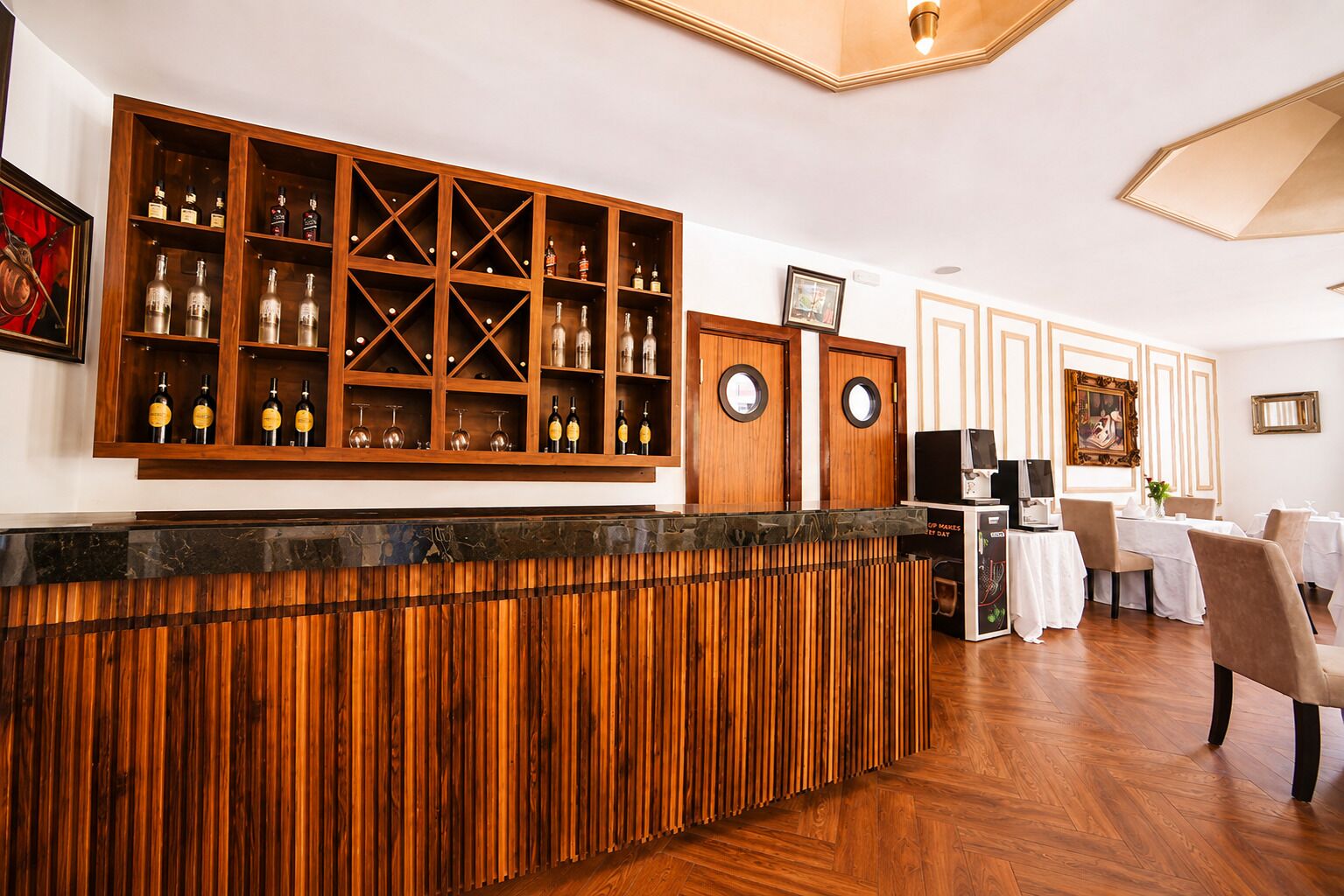 Un espace bar avec des étagères en bois et un comptoir, un espace repas avec des tables et des chaises, et un téléviseur posé sur un meuble.