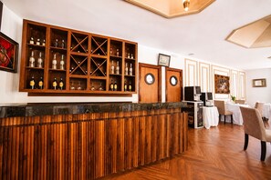 Una zona de bar con estantes de madera y una barra, un comedor con mesas y sillas, y un televisor sobre un soporte.
