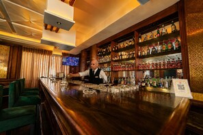Zona de bar con un cantinero, estantes llenos de botellas de licor y taburetes.
