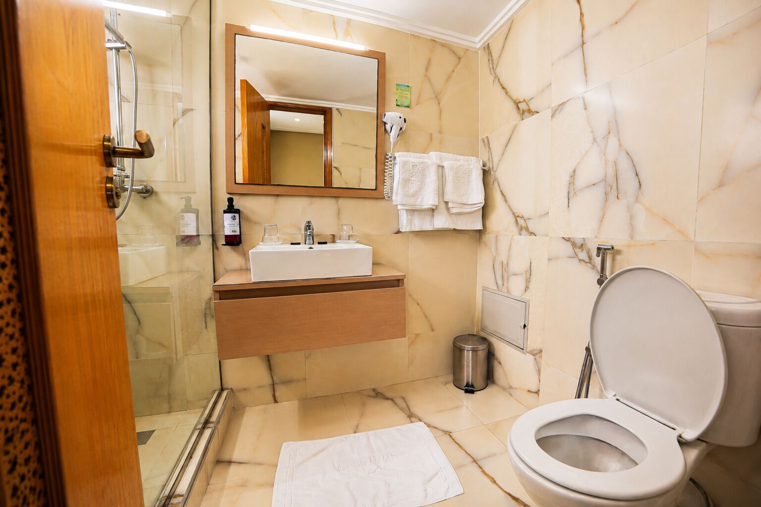 A bathroom with a marble floor, a sink with a mirror above it, a toilet, and a shower area.